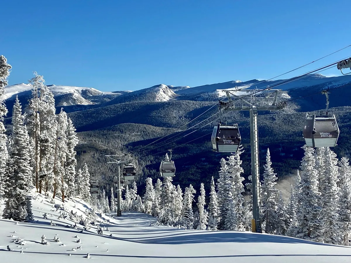 A picturesque exterior shot featuring ski lift gondolas ascending above snow-laden trees, with breathtaking mountain vistas in the background. It embodies the allure of adventure and the convenience of slope-side access.