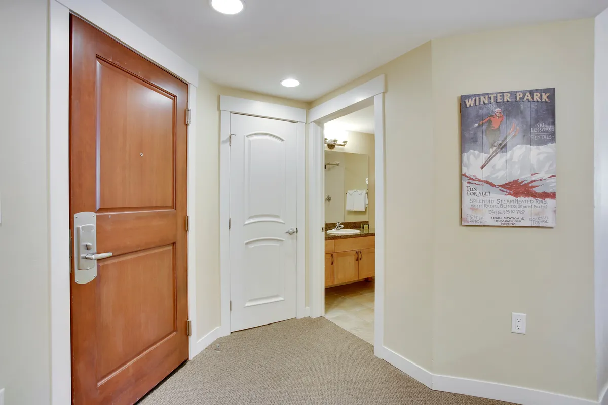 The entryway to a resort condo, with a welcoming main door, interior bathroom door, and a nostalgic Winter Park poster. The scene captures the transition from outdoor adventure to indoor comfort, emphasizing the resort as a launchpad for exploration.