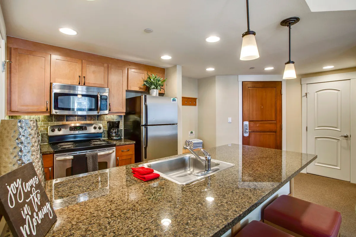 This image showcases a modern kitchen featuring granite countertops, stainless steel appliances, and a decorative sign. The kitchen layout appears open and welcoming, with visible elements that suggest a space designed for both cooking and entertaining. The countertop provides ample prep space, and the appliances are ideal for preparing family meals or gourmet dinners.
