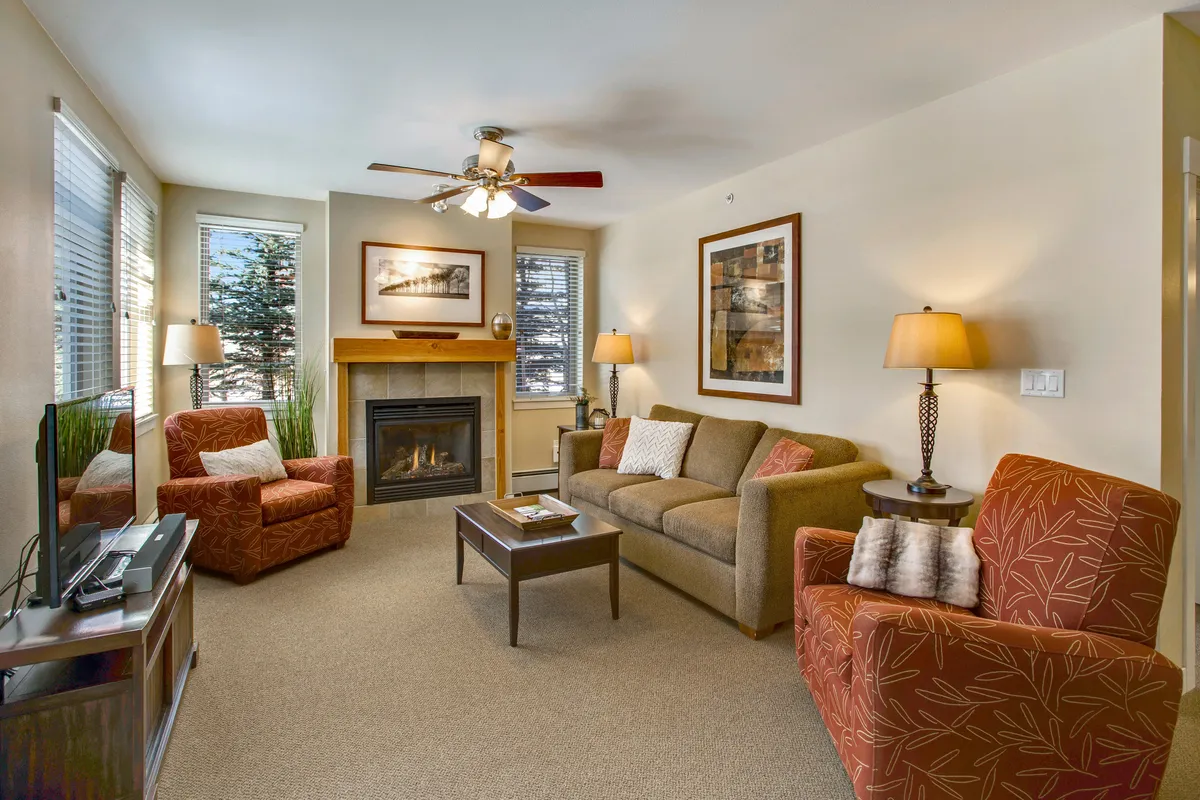 The image features an inviting interior lounge area with a prominent fireplace, comfortable sofas and armchairs, and tasteful artwork. The mood is warm and sociable, suggesting a perfect setting for unwinding or sharing stories after a day outdoors.