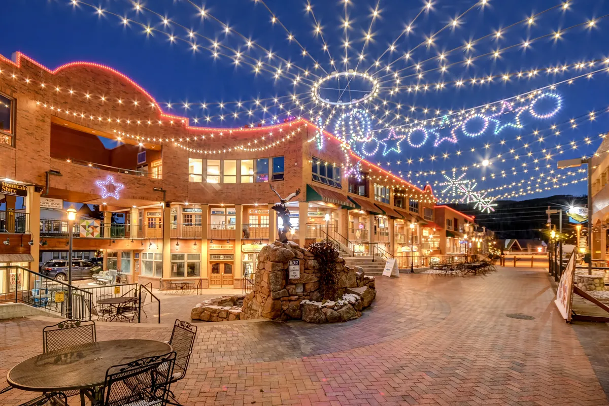Evening ambiance is set with string lights twinkling overhead, decorative stars, and a central fountain surrounded by outdoor seating. The festive, communal mood encourages gathering and socializing, aligning with the section's mention of grilling with friends and relaxing in a shared outdoor environment.