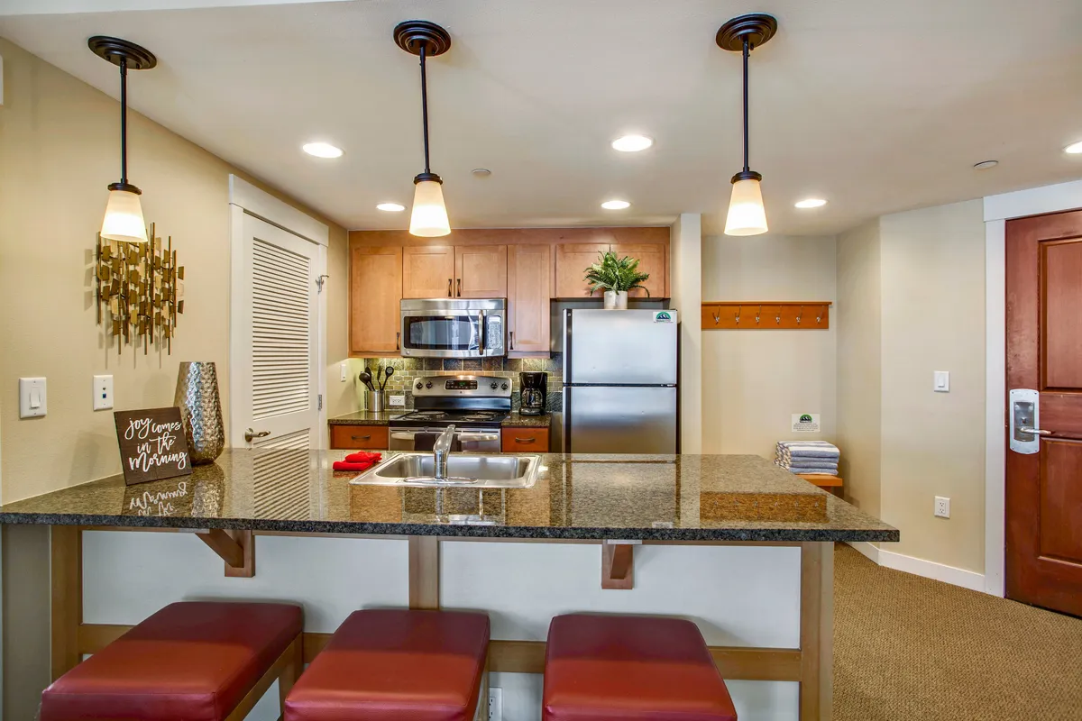 This photo highlights a kitchen island with seating, stainless steel appliances, and decorative wall art, all within a warmly lit, inviting space. The presence of bar stools and the open-concept design connect the kitchen to the dining area, showcasing a space intended for both cooking and socializing.