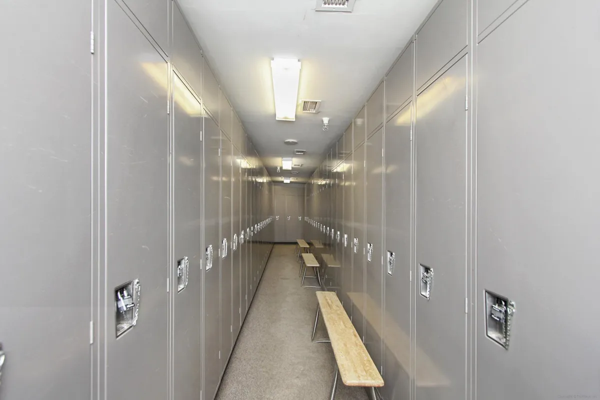 An interior view of a secure storage area featuring metal lockers and benches under overhead lighting. The space is practical and organized, ideal for storing ski and bike gear after a day of mountain activities.