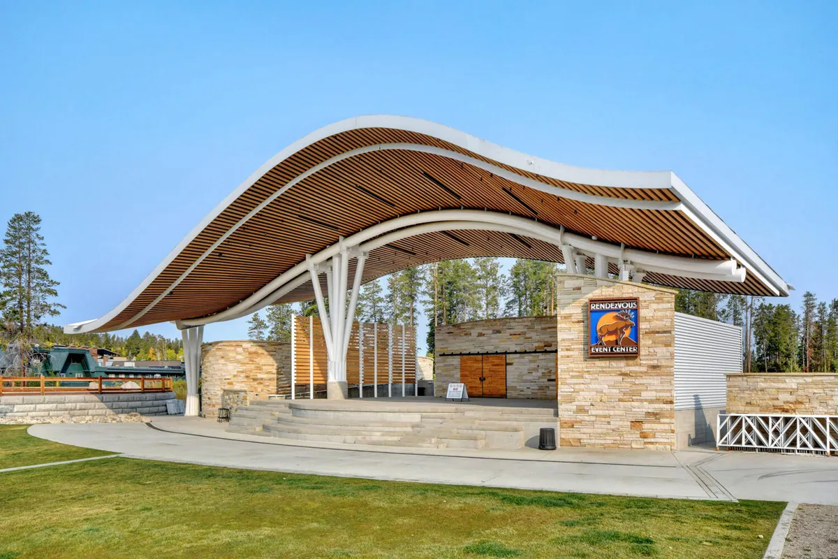 An open-air stage with a distinctive curved roof and stone facade, set up for community events and live performances. Event signage and gathering spaces suggest a festive, communal environment ideal for group outings or evening entertainment.